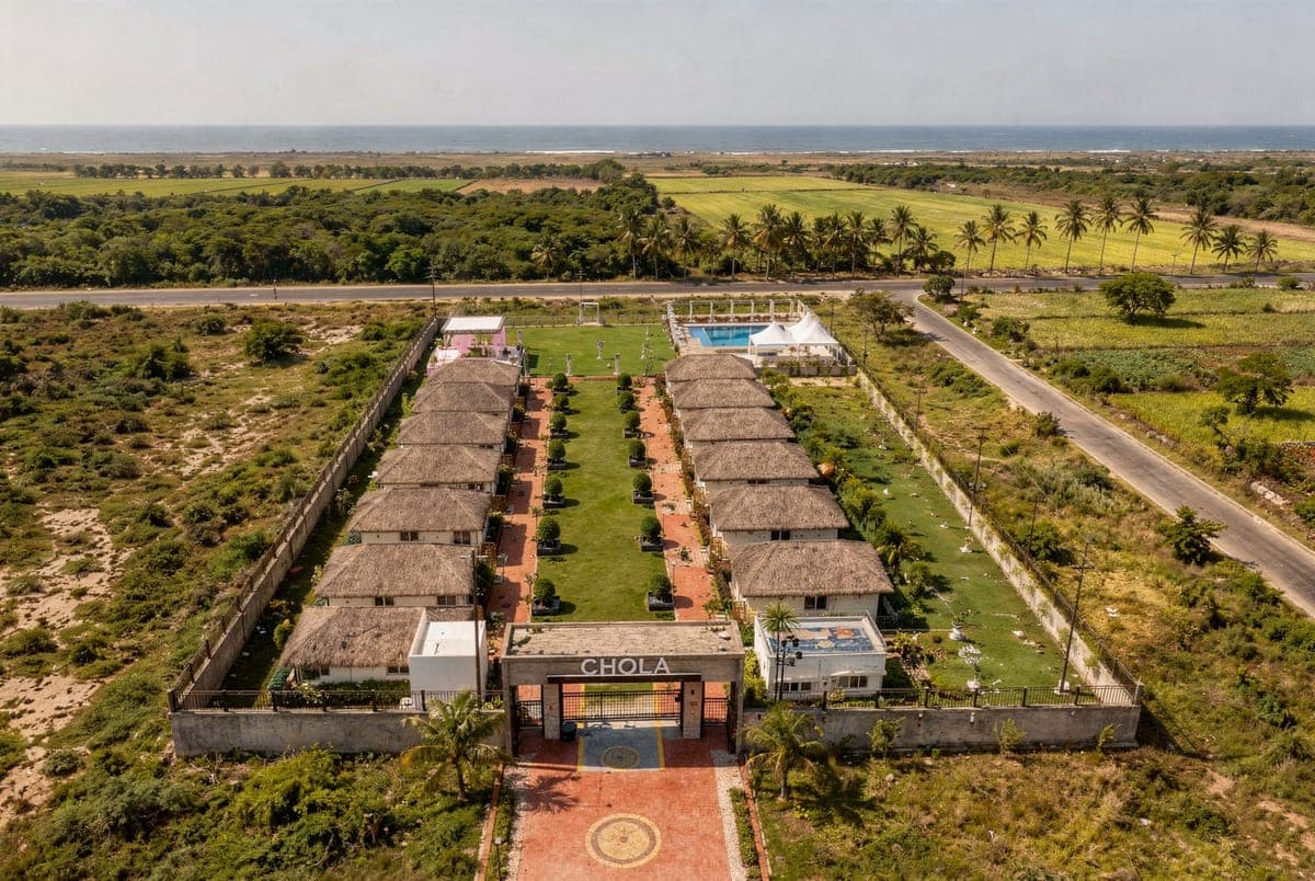 The whole resort from the air on a clear morning: two rows of thatched cottages either side of the lawn, the pool at the far end and the sea beyond the fields.